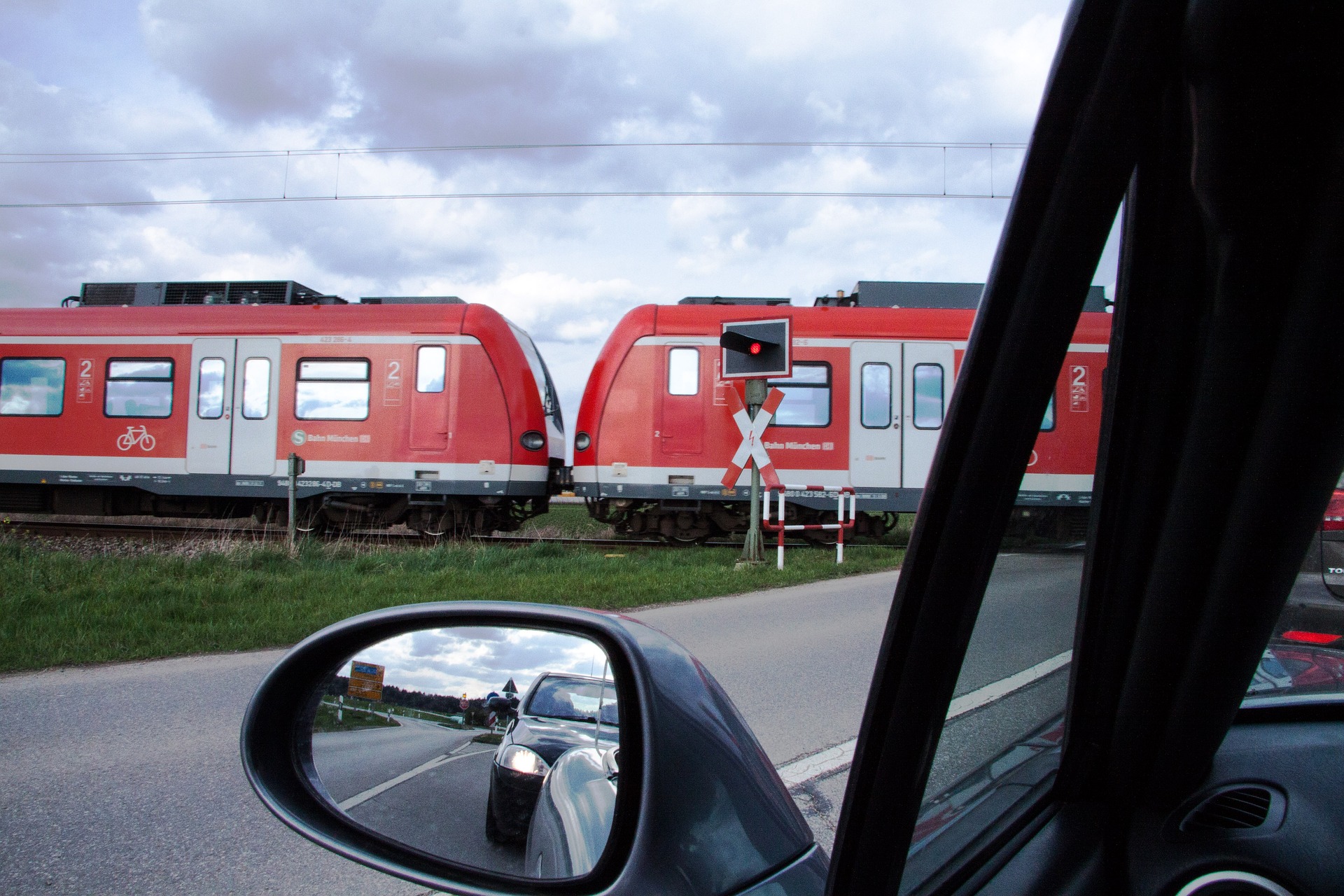 Blick aus einem Pkw, der vor einem geschlossenen Bahnübergang gehalten hat, auf die durchfahrende rote S-Bahn