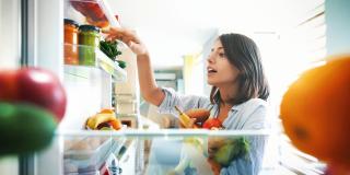Eine junge Frau, die frische Lebensmittel in einen Kühlschrank räumt